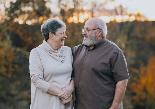 Photo of older couple smiling at each other, with a sunset behind some trees